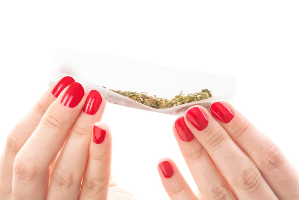 Rolling paper with weed in it held by two pairs of hands.