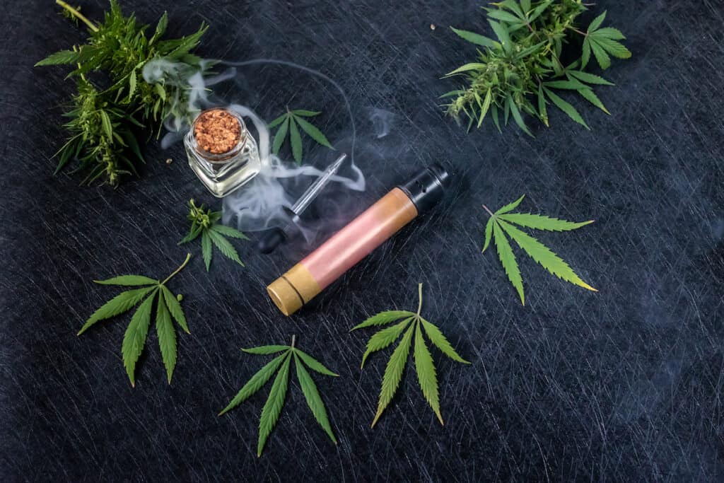 cannabis accessories on black table with leaves around them