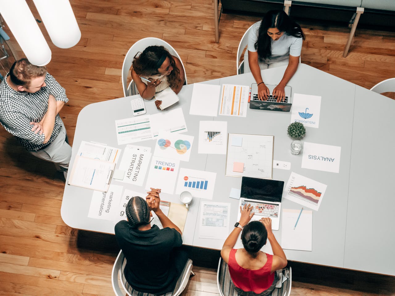 Diverse marketing team collaborating around a table covered with strategy documents, charts, and laptops in a modern office.