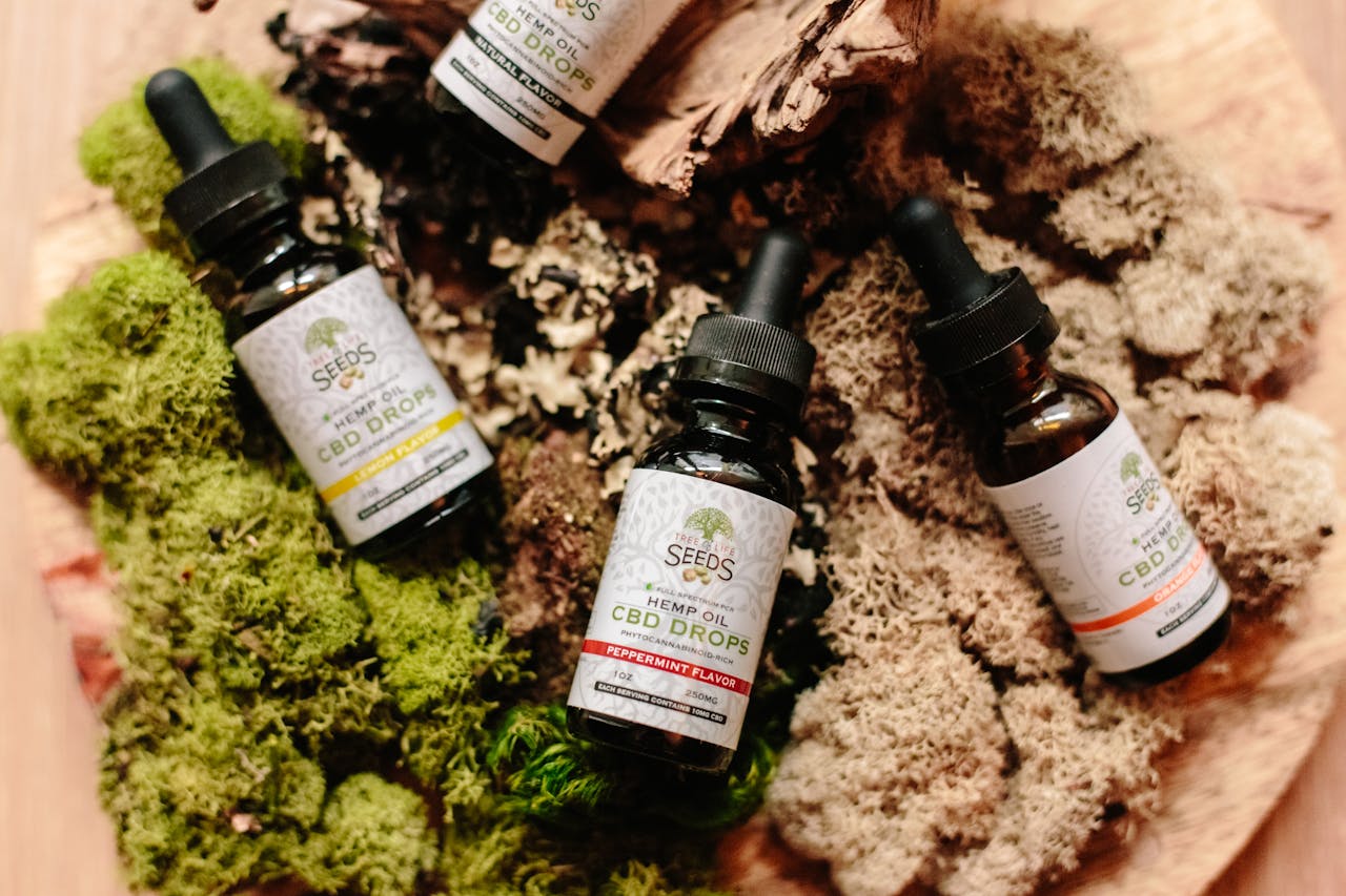 Four Seeds Hemp Oil CBD Drops tincture bottles in peppermint, lemon, orange, and natural flavors arranged on decorative moss