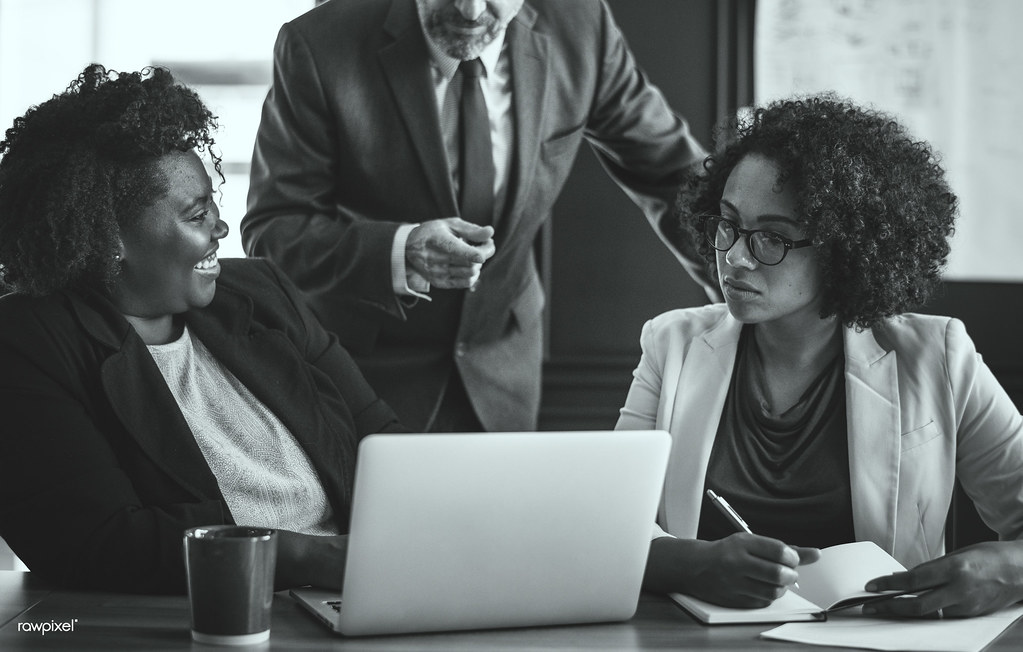 Black and white photo of three colleagues reviewing work on a laptop