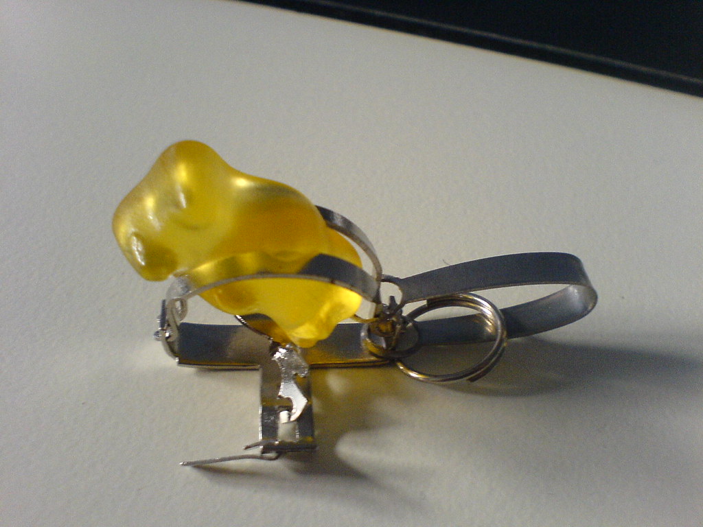 Yellow gummy bear held by a metal clip on a white surface