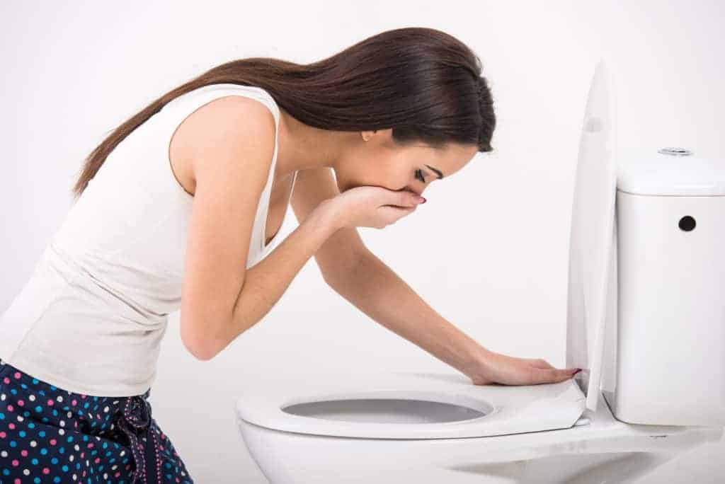 Young woman vomiting into the toilet bowl in the early stages of pregnancy or after a night of partying and drinking. CBd oil for nausea.
