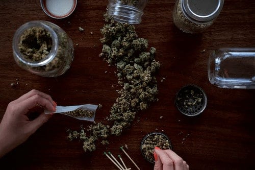 marijuana buds on table next to rolling paper and weed grinder, consume marijuana