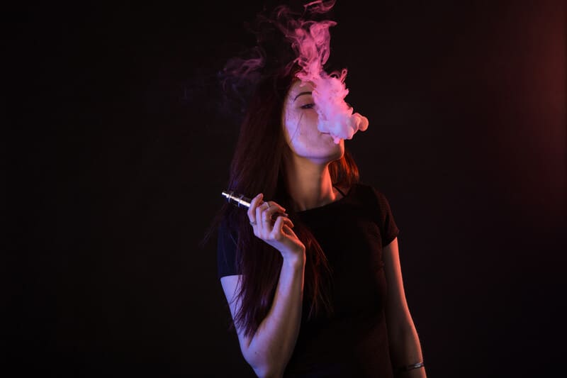 women blowing smoke holding a pink dab pen